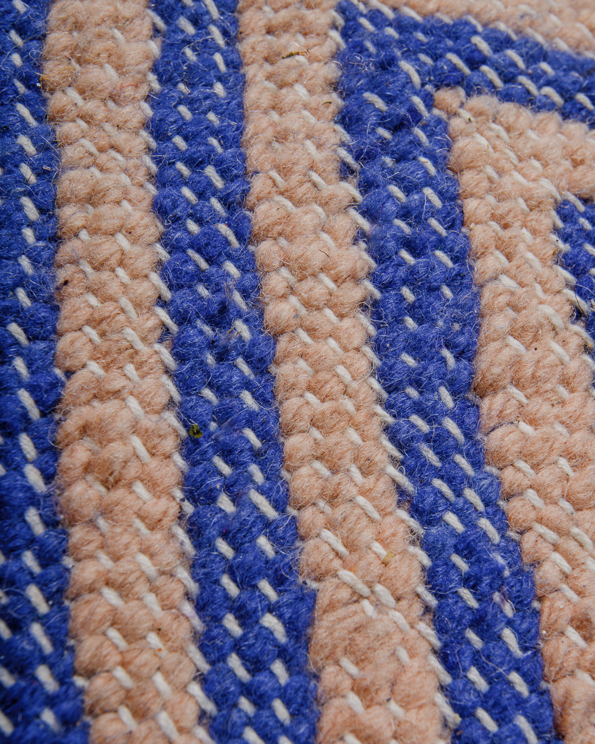Close-up of blue and rose coloured kelim with white cotton stitching.